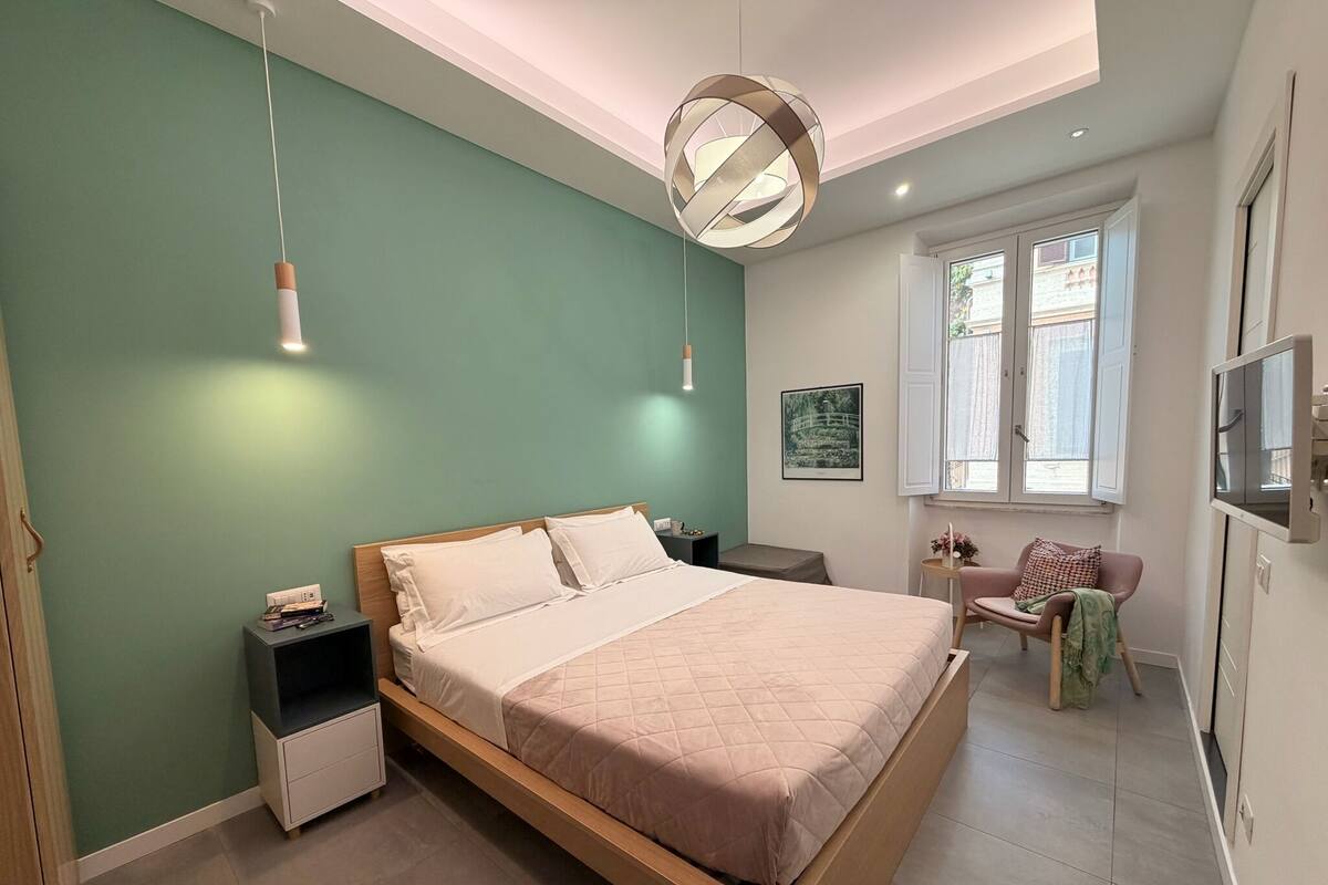 A modern bedroom with a bed, bedside tables, a chair, a window, and a TV.