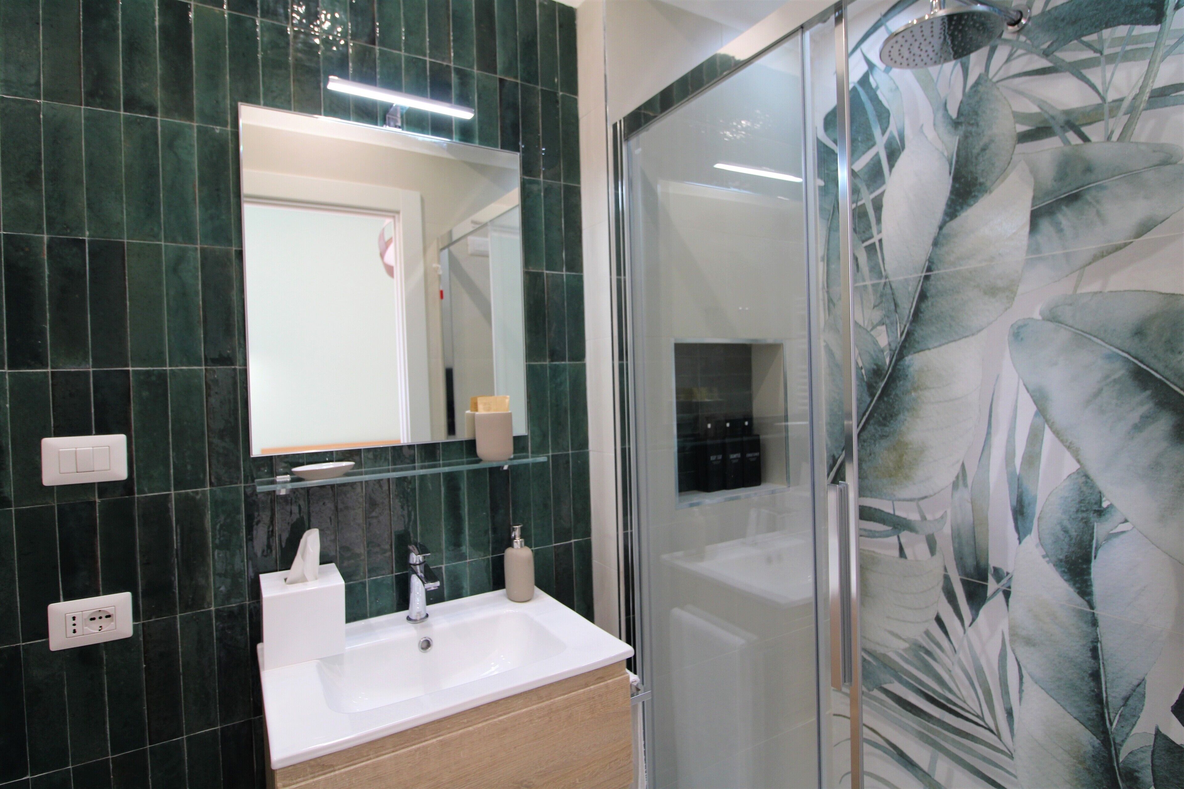 A bathroom with a white sink, mirror, and green-tiled walls.