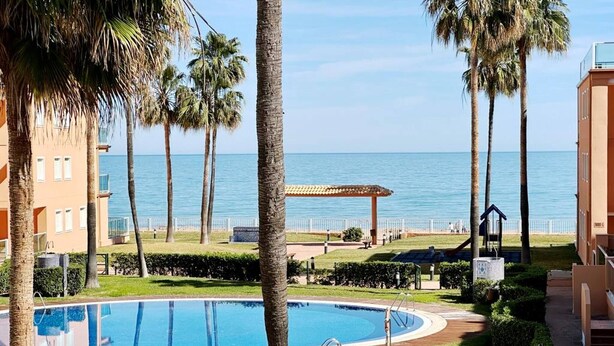 A swimming pool with a wooden deck, palm trees, and a view of the sea. - Beautiful and comfortable apartment  with communal pool in Denia, Costa Blanca, Spain for 6 persons (Denia)