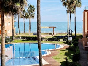 Une piscine avec une terrasse en bois, des palmiers et une vue sur la mer.