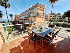 Un balcon doté d’une table et de chaises en verre, offrant une vue sur une piscine et un immeuble comportant de nombreux balcons.