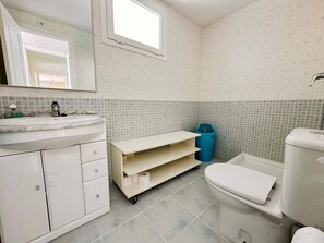 Une salle de bain avec un lavabo blanc, un miroir, des toilettes et une petite fenêtre.