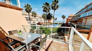 A balcony with a glass table and chairs, overlooking a pool and palm trees. - Beautiful and comfortable apartment  with communal pool in Denia, Costa Blanca, Spain for 6 persons (Denia)
