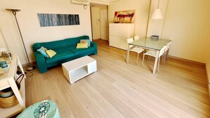 A living room with a green sofa, a white coffee table, a dining table with chairs, and a painting on the wall. - Beautiful and comfortable apartment  with communal pool in Denia, Costa Blanca, Spain for 6 persons (Denia)