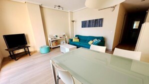 A modern living room with a flat-screen TV, a glass dining table, a teal sofa, and a white coffee table. - Beautiful and comfortable apartment  with communal pool in Denia, Costa Blanca, Spain for 6 persons (Denia)