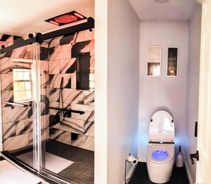 A bathroom with a glass shower enclosure, a white toilet with a blue light, and a marble-patterned wall. - Glen Mary Apartments (Bar Harbor)