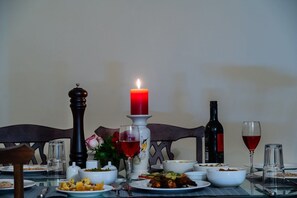 A dining table set with plates of food, glasses of red wine, a candle, and a salt and pepper shaker. - Sajjan Niwas (Jodhpur)