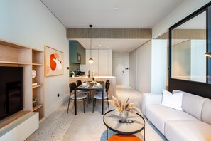A modern living room with a sofa, a coffee table with a vase, and a dining area with chairs and a table. - Modern 1BR w/ Balcony in Business Bay (Dubai)
