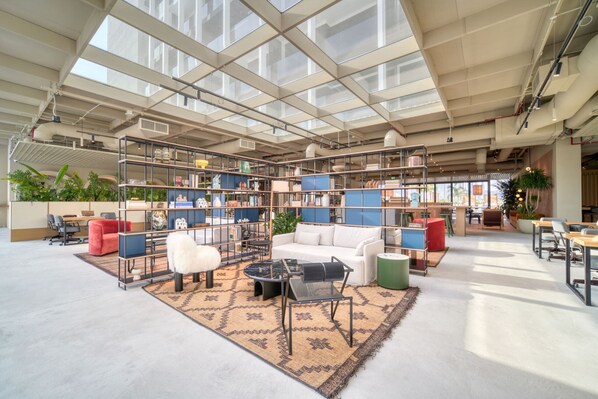 A spacious indoor area with a high ceiling, large windows, and a variety of seating arrangements including sofas, chairs, and tables.
