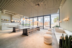 Un interior moderno con una larga mesa de comedor, zona de estar y ventanas amplias que ofrecen vistas de la ciudad.