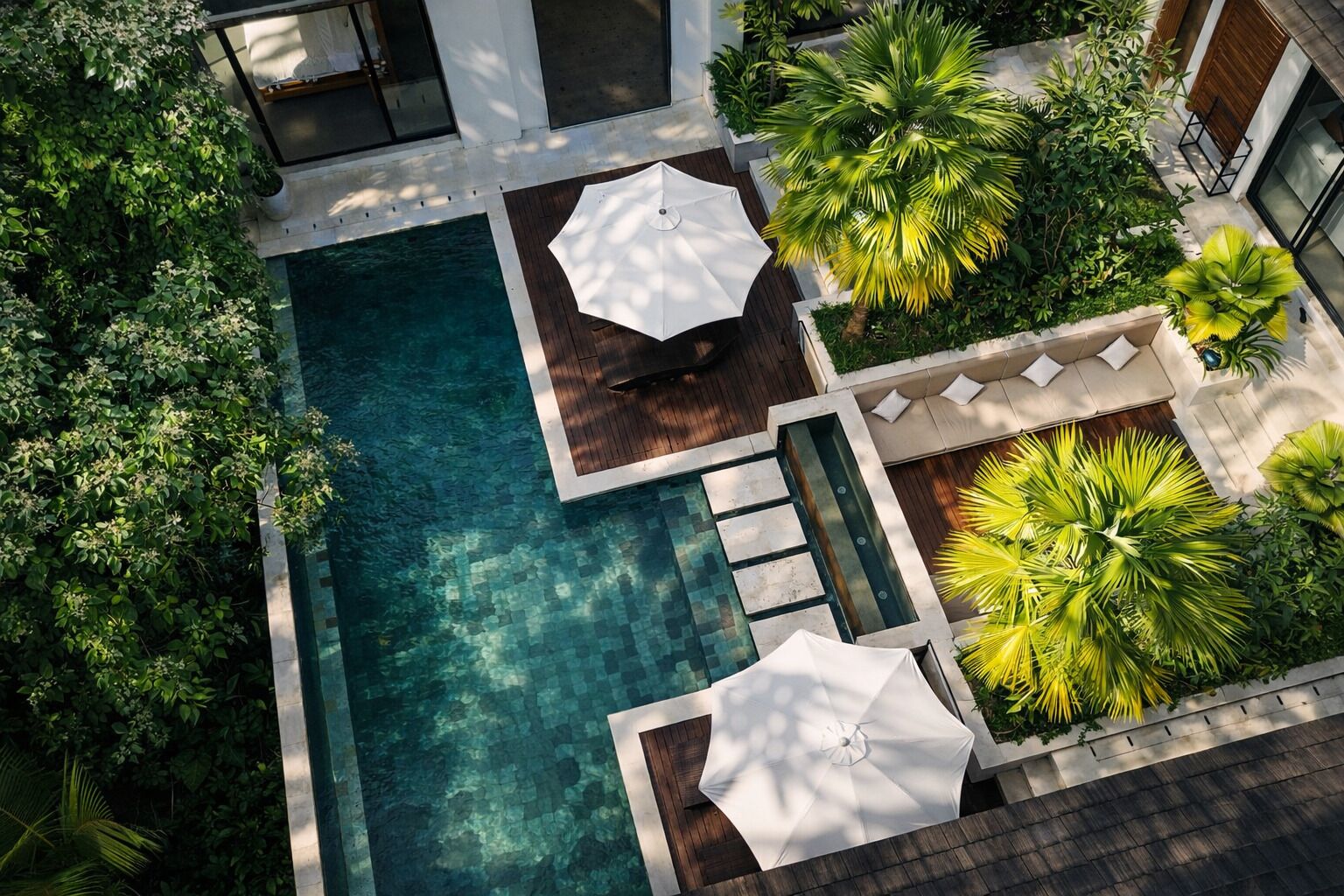 An aerial view of a modern outdoor pool area with a rectangular pool, wooden deck, and white umbrellas.