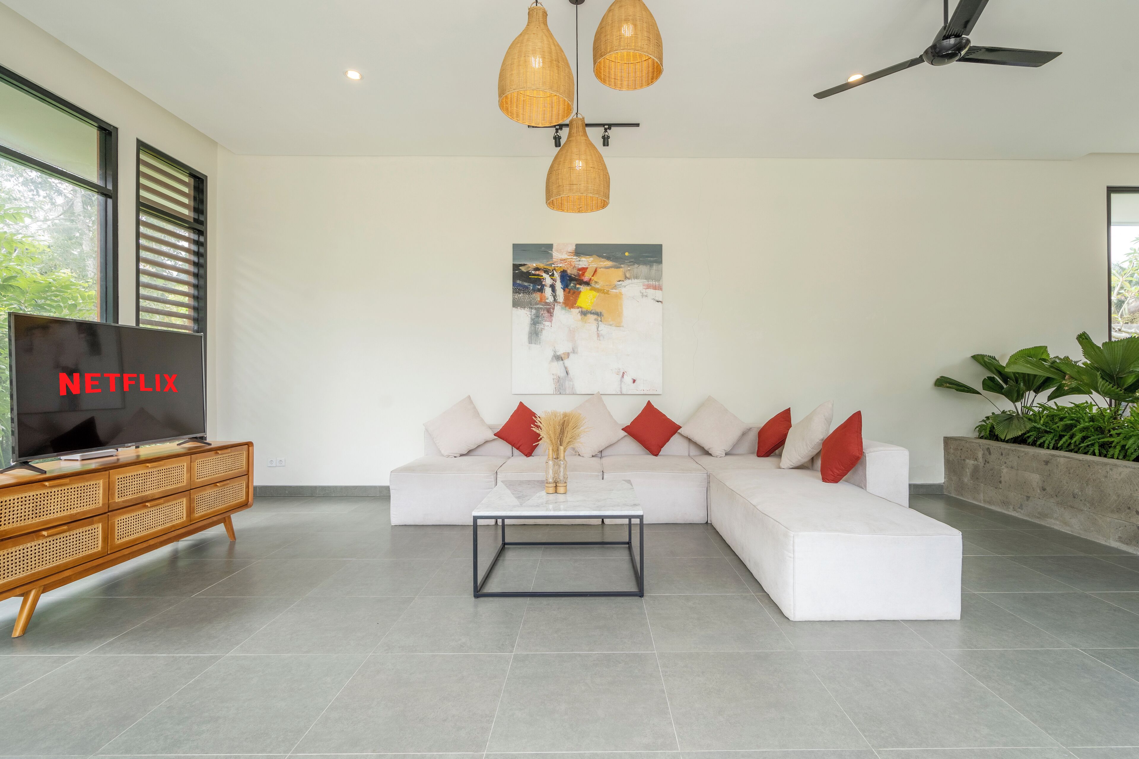 A modern living room with a sectional sofa, a coffee table, a TV on a wooden console, and a ceiling fan.
