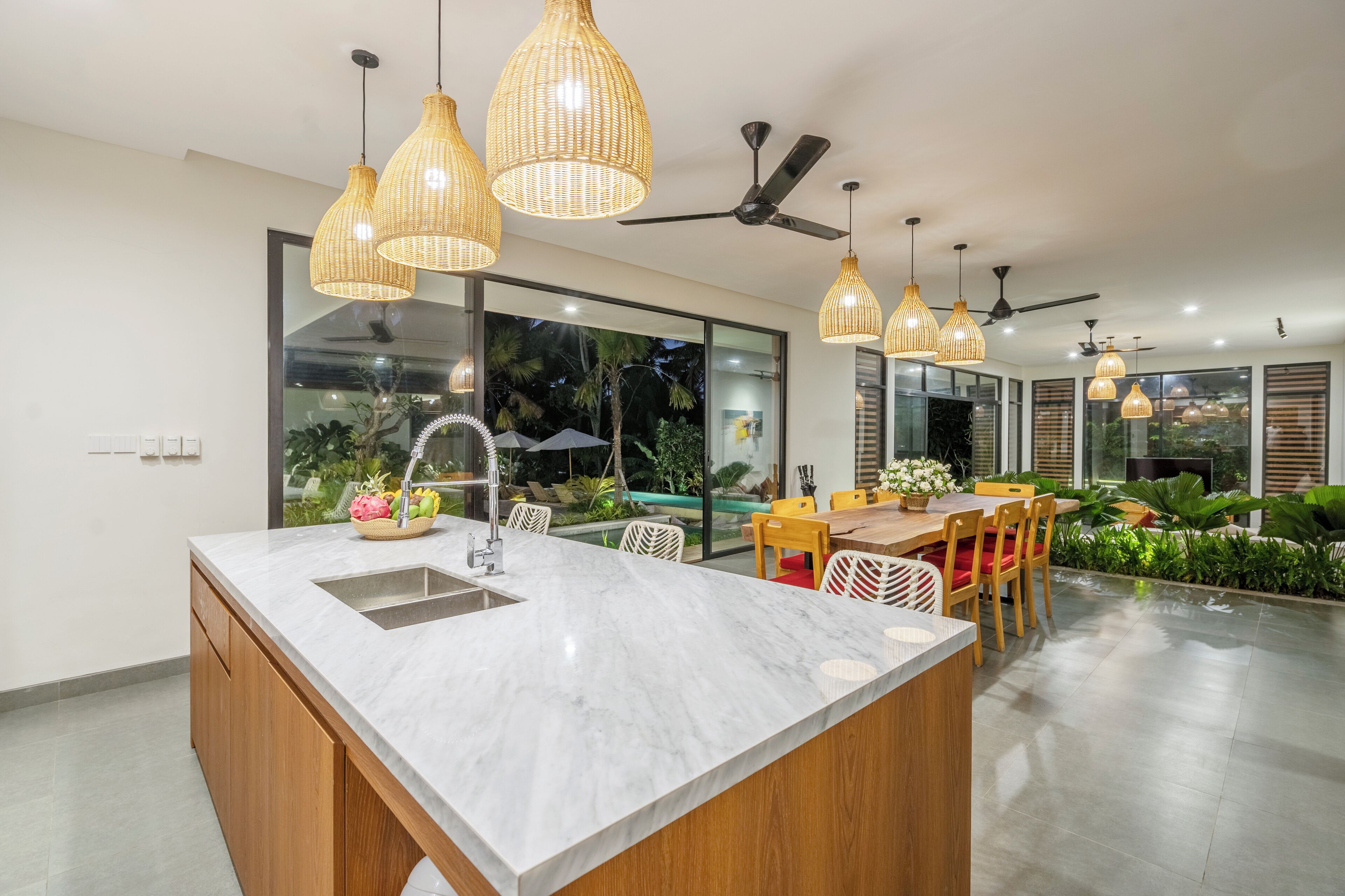 A modern kitchen with a large island, pendant lights, and a view of a pool and greenery.