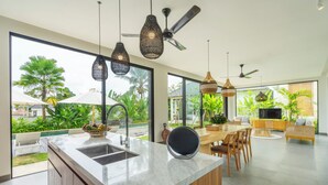 Une cuisine moderne dotée d’un grand îlot central, de luminaires suspendus et offrant une vue sur l’extérieur.