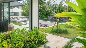 Une maison moderne à l’extérieur en verre, dotée d’une piscine et agrémentée d’une végétation tropicale luxuriante.