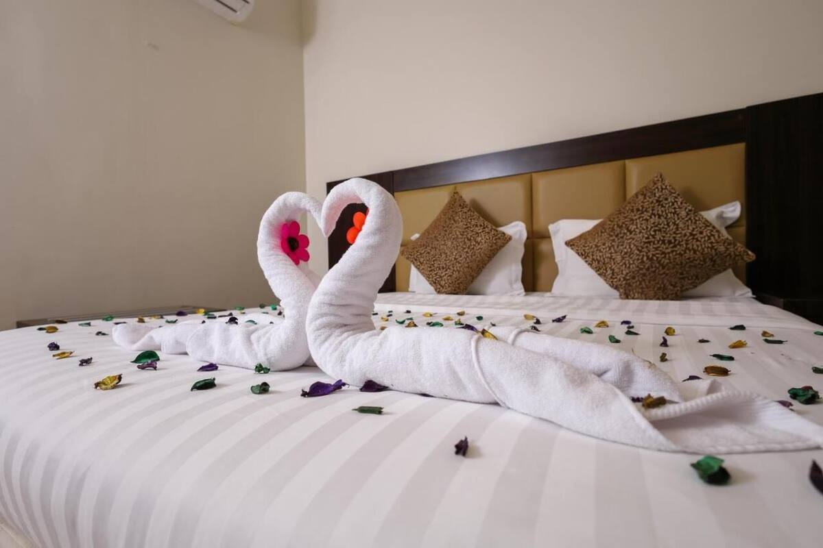 A bed with white striped bedding, two decorative swan-shaped towels, and scattered flower petals.