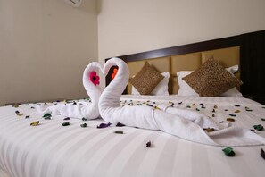 Een bed met wit gestreepte lakens, twee decoratieve zwaanhanddoeken en verspreide bloemblaadjes.