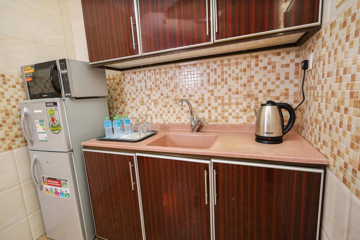 A kitchen with a microwave, refrigerator, sink, and a kettle.