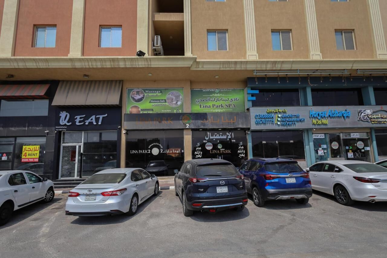 Un immeuble à plusieurs étages abritant divers commerces, notamment un spa, un restaurant et un parking où sont stationnées plusieurs voitures.