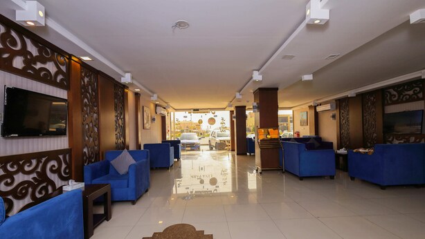 A hotel lobby with blue sofas, a TV mounted on the wall, and a clear view of the parking area outside. - lina 2 (Dammam)
