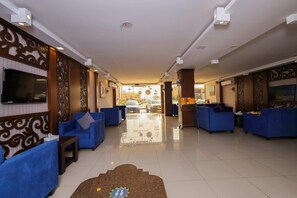 Een hotel lobby met blauwe banken, een aan de muur bevestigde televisie en een helder uitzicht op het parkeerterrein.
