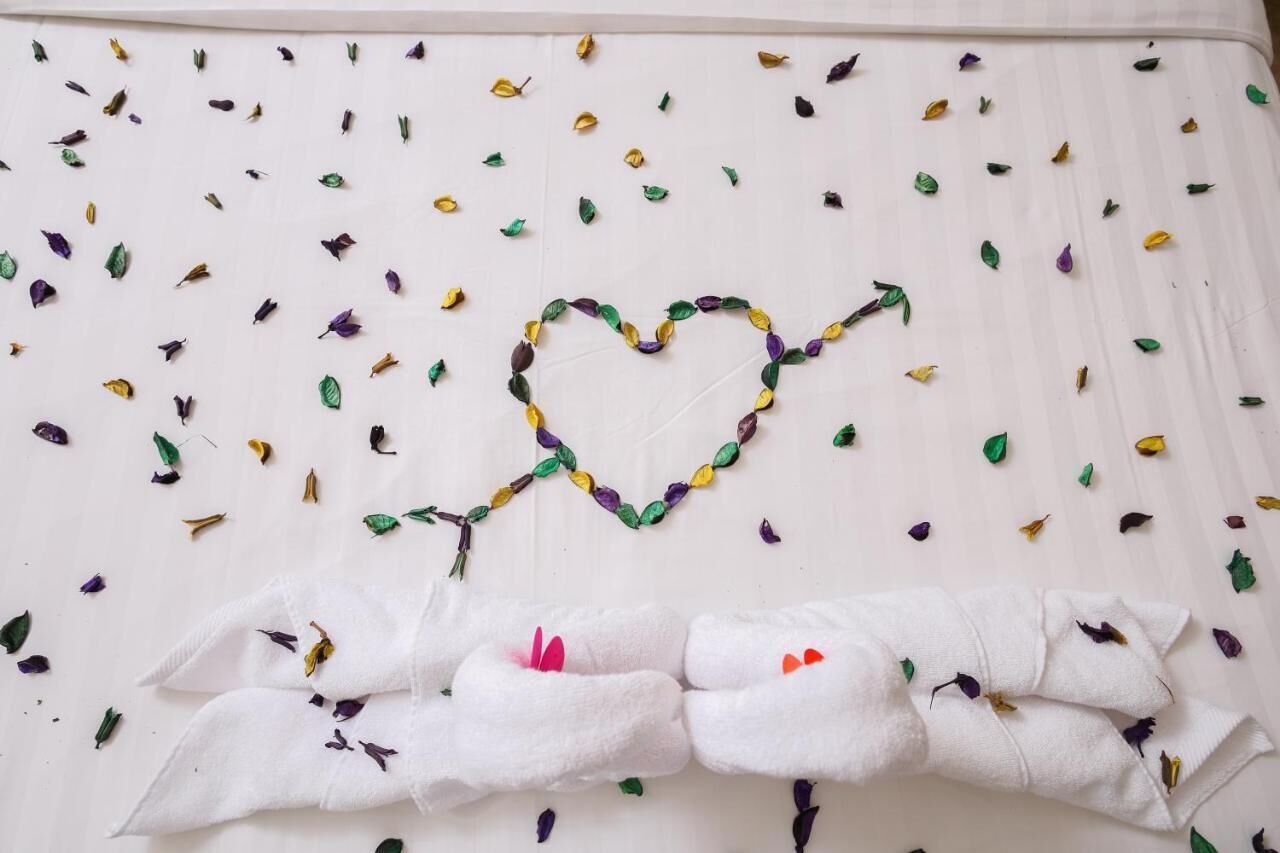 A white wall with a heart-shaped decoration made of leaves and a white towel with a pink ribbon.