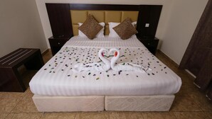 A neatly made bed with a heart-shaped towel arrangement, two decorative pillows, and a bedside table. - lina 2 (Dammam)