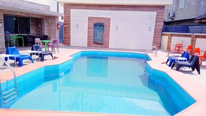 A rectangular swimming pool with a tiled edge, surrounded by outdoor seating with chairs and tables.
