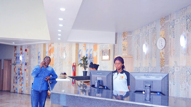 A reception desk with two monitors, a clock, and a plant.