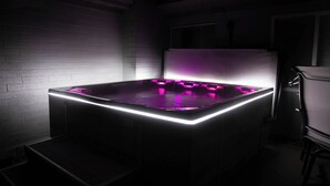 Een hottub met LED-verlichting in een gedimde ruimte met een bakstenen muur en een raam.