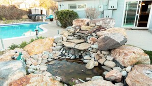 Een zwembad met een waterval en een terras met tuinmeubilair.