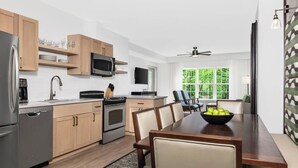 A modern kitchen with wooden cabinets, stainless steel appliances, a dining area with a table and chairs, and a view of greenery through the window. - Unwind in Style: Marriott Fairway Villas (Galloway)