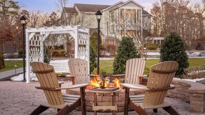 An outdoor seating area with four Adirondack chairs around a small table with a fire, set against a backdrop of a house and trees. - Unwind in Style: Marriott Fairway Villas (Galloway)