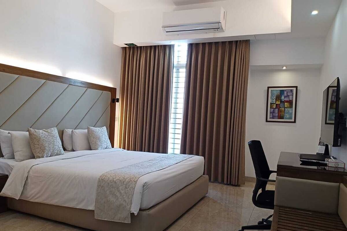 A hotel room with a large bed, a desk with a chair, and a window with curtains.