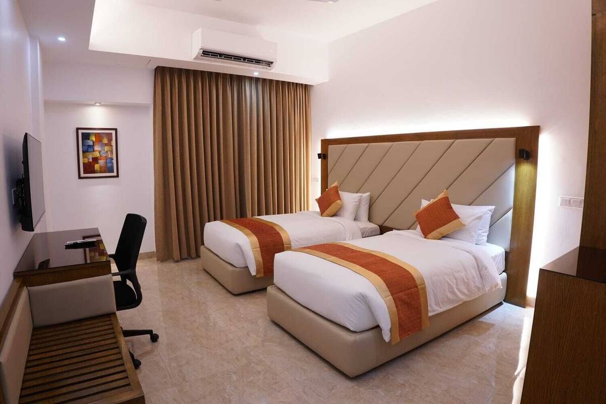A hotel room with two beds, a desk, a chair, a TV, and a large window with curtains.
