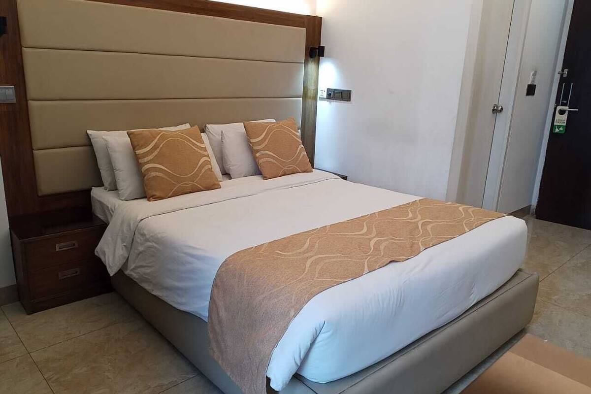 A neatly made bed with a headboard, a bedside table, and a door in the background.