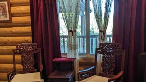L’intérieur d’une cabane en rondins, avec deux fauteuils en bois richement décorés, une petite table et un tapis à motifs.