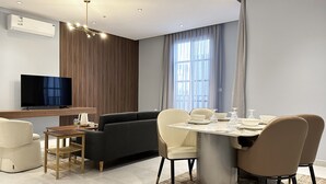 Ein modernes Wohnzimmer mit Flachbildfernseher, einer Couch, einem Esstisch mit Stühlen und einem großen Fenster mit Vorhängen.