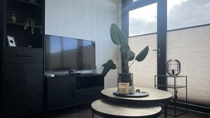 A modern living room with a flat-screen TV, a round table with a vase and a cup, a potted plant, and a chair. - De Zeeparel by Interhome (Scherpenisse)