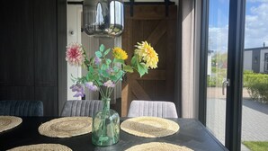 A modern dining area with a glass table, woven placemats, and a vase of flowers. - De Zeeparel by Interhome (Scherpenisse)