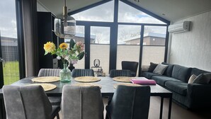 A modern dining area with a table set for six, surrounded by grey upholstered chairs. A vase with flowers is placed on the table, and a black birdcage is visible in the background. - De Zeeparel by Interhome (Scherpenisse)