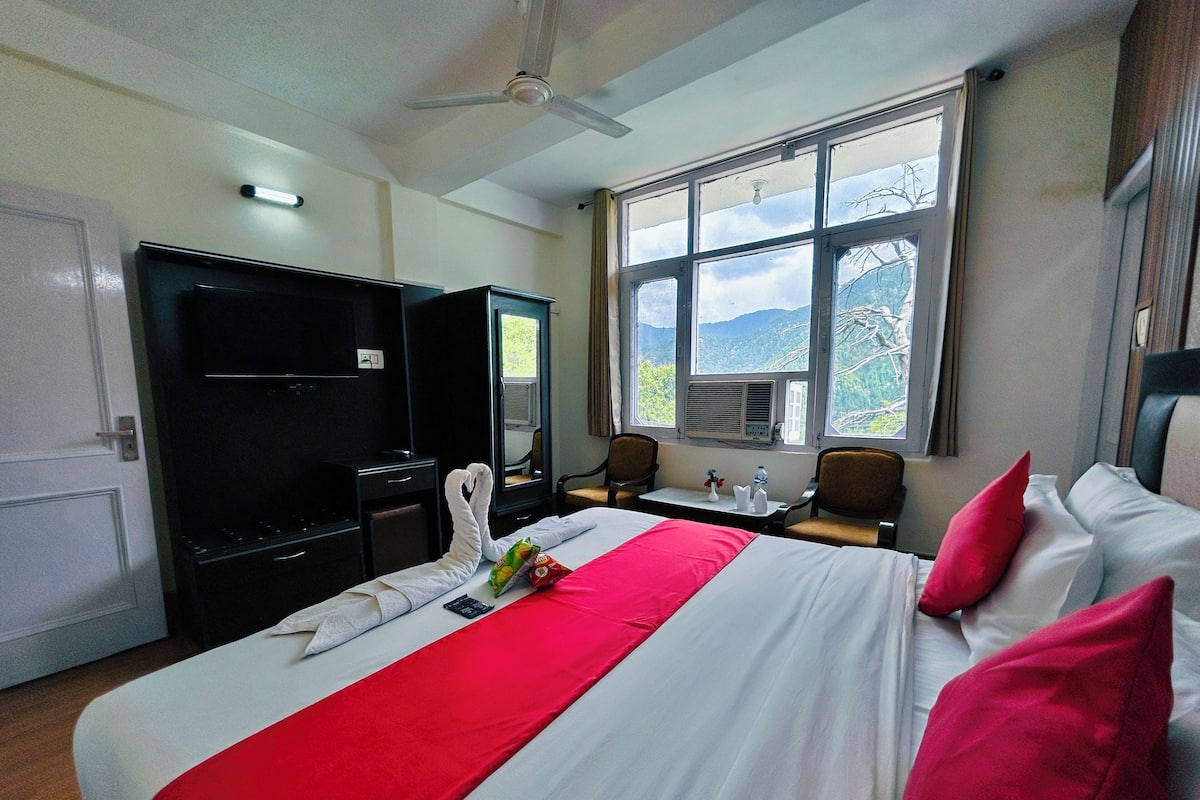 Une chambre d’hôtel équipée d’un lit, d’un bureau, d’une chaise, d’une télévision et d’une fenêtre donnant sur la montagne.
