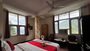 A hotel room with a bed, a desk, a chair, a TV, and large windows with a mountain view. - Hotel Eagle Nest Central Heated  (Dalhousie)