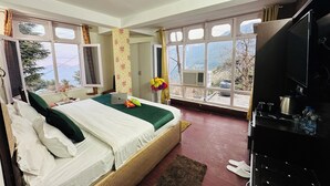 A bedroom with a bed, a desk, a chair, a TV, and a window with a view of the mountains. - Hotel Eagle Nest Central Heated  (Dalhousie)
