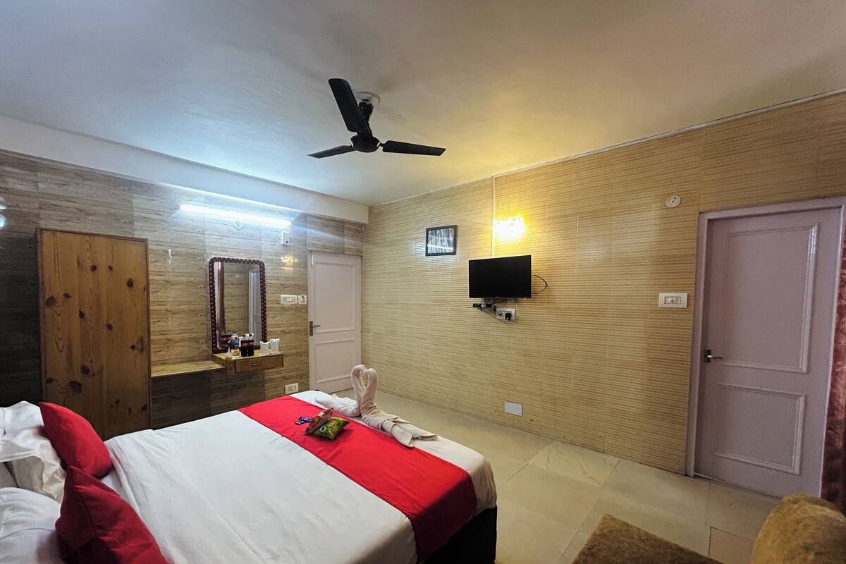 Une chambre d’hôtel avec un lit, un ventilateur de plafond, un téléviseur fixé au mur et une porte.