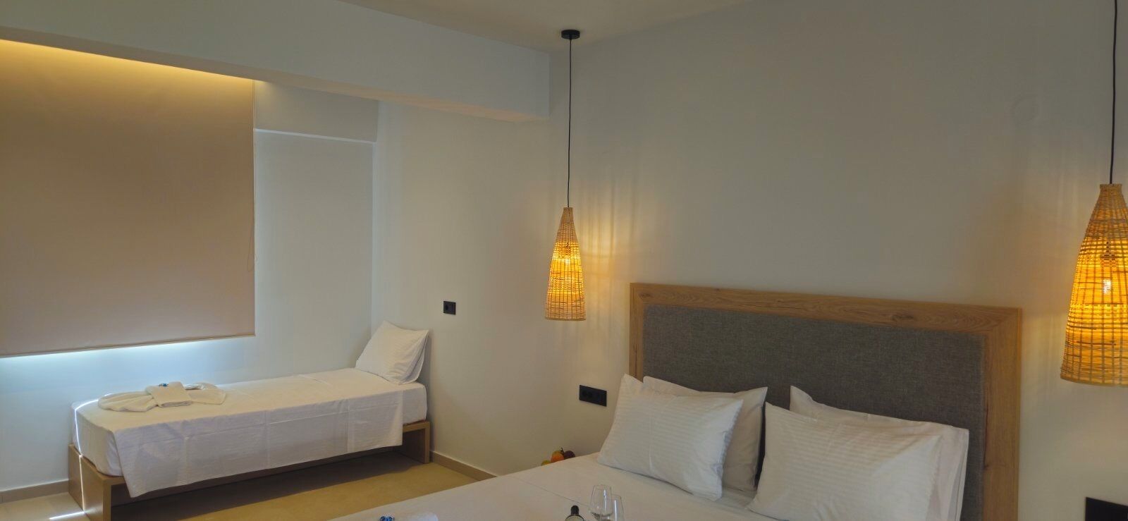 Habitació d'hotel amb un llit individual, un llit més petit i una tauleta de nit amb una làmpada.