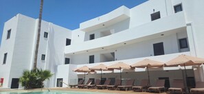 A modern building with a pool area, including sun loungers and umbrellas. - Aegean View Hotel (Rethymno)