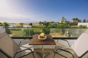 A balcony with a wooden table and two chairs, overlooking a beach and palm trees. - Aegean View Hotel (Rethymno)
