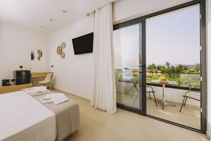 A hotel room with a bed, a desk, a TV, and a balcony with a view of the sea. - Aegean View Hotel (Rethymno)