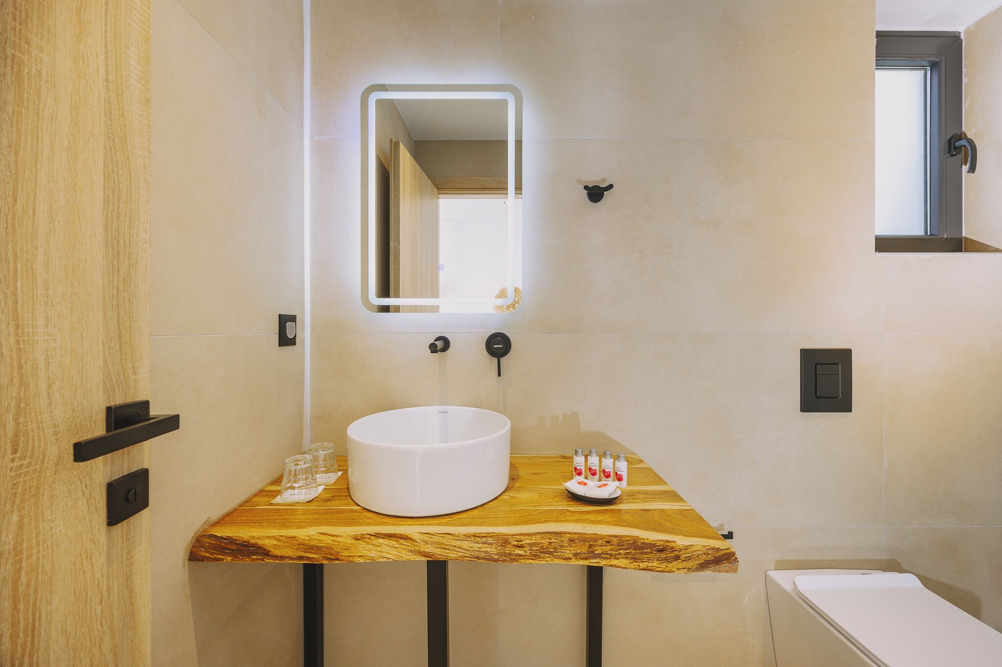 A bathroom with a wooden vanity, a round sink, a mirror with a light, and a towel rack.